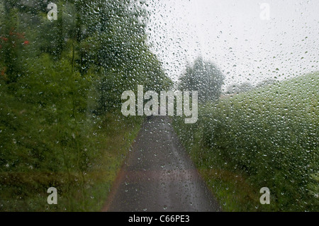 View from the top deck of bus as it travels along a country lane on a rainy day. the rain drops can be seen on the window Stock Photo