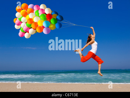 Beautiful and athletic girl with colorful balloons jumping on the beach