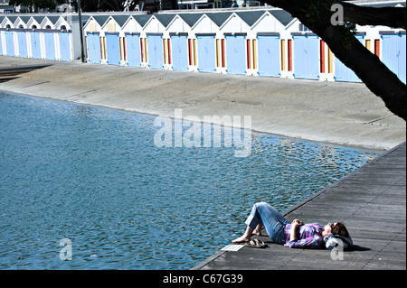 Girl Sunbathing by a  Line of Boat Sheds at The Royal Port Nicholson Yacht Club Wellington North Island New Zealand NZ Stock Photo