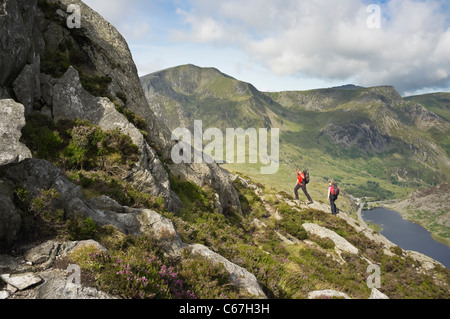 Hikers climb mount Tryfan north ridge above Llyn Ogwen lake in mountains of Snowdonia with Y Garn beyond Ogwen Valley North Wales UK Stock Photo