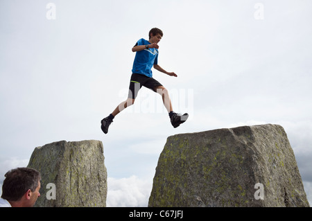 Teenager jumping across gap between Adam and Eve stones on Mount Tryfan mountain top summit in Snowdonia National Park North Wales UK Britain Stock Photo