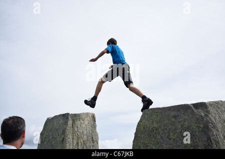 Teenager jumping between Adam and Eve stones on Tryfan summit in Snowdonia National Park. Ogwen, Conwy. North Wales, UK. Stock Photo