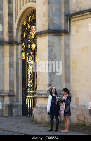 two Asian tourists in front of the gate to The Quadrangle of All Souls College opposite Radcliffe Camera Oxford UK Stock Photo