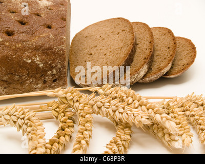 ein angeschittenes Schwarzbrot, davor liegen Weizenähren | a sliced Brown Bread in front are wheat ears Stock Photo