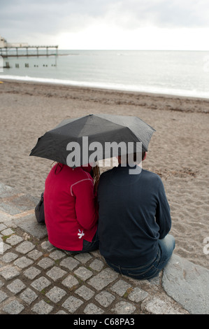 A couple on holiday sheltering under an umbrella in the rain, august summer afternoon, Aberystwyth Wales UK Stock Photo