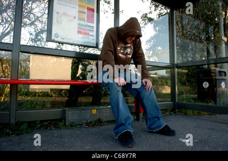 Young man wearing a hoodie sitting in bus shelter = posed by model Stock Photo