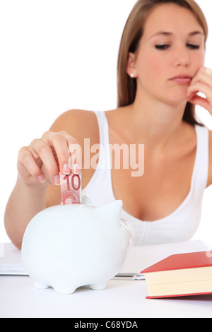 Attractive young student puts money in her piggy bank. All on white background. Stock Photo