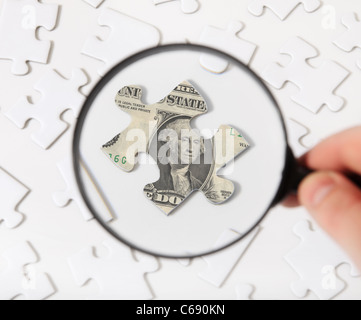 Person using magnifier to check piece of puzzle with topic of a dollar note. Stock Photo