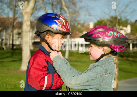 Diverse young person people child helping another helpful helpfully girl 6-8 year old fastens helmet adoption Hispanic brother 4-5 years  MR  © Myrleen Pearson Stock Photo