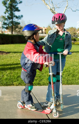 Wearing jacket Young girl and pre-K Hispanic boy on scooters at park child helping another  MR © Myrleen Pearson Stock Photo