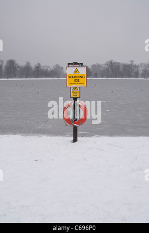 warning ice sign at the round pond in London's Hyde Park after snow with ice on the water Stock Photo