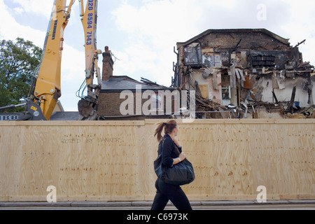 A smartly dressed woman with a pony tail walks past a building on Tottenham High Road burnt down in the London summer riots. Stock Photo