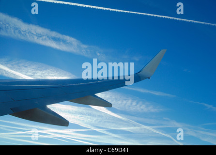 Wing of airliner on a blue sky full of exhaust planes traces generating cirrus clouds (Ci) formation during wintertime, France Stock Photo