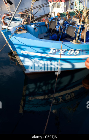 The blue and white hull of FY95 fishing boat reflected in the water at Sutton Harbour, Barbican, Plymouth. Stock Photo