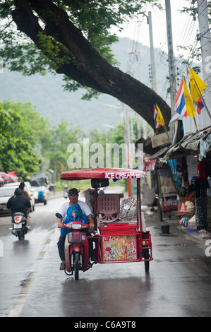 Ice Cream seller with a child riding a motorized tricycle in the rain Kanchanaburi Thailand Stock Photo