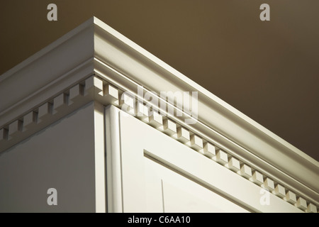 The top crown moulding dentil detail on some creme-color painted solid wood kitchen cabinets. Stock Photo