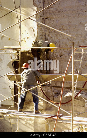two workers stand on scaffold while demolishing building Stock Photo