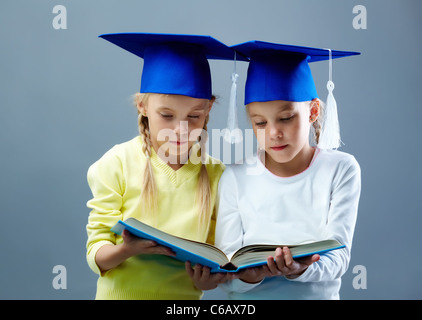 Portrait of lovely twin girls in hats with tassels reading book Stock Photo