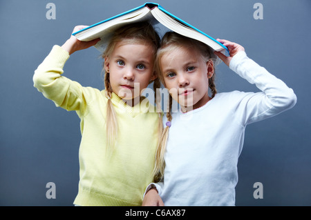 Portrait of lovely twin girls holding open book over heads Stock Photo