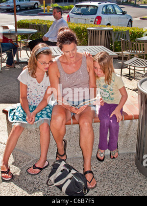 A mother reads to her two daughters on a sunny afternoon at an outdoor cafe in Laguna Niguel, CA. Stock Photo