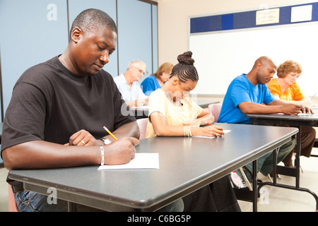 Class of adult college students taking a test. Focus on guy in front left. Stock Photo