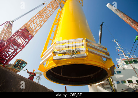 A crane lifts a transition piece onto the deck of a barge, ready to take out to the Walney offshore wind farm Stock Photo