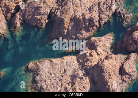 AERIAL VIEW. Couple kayaking in a narrow waterway in a landscape of red volcanic rock. Esterel Massif, Cap Dramont, Saint Raphaël. French Riviera. Stock Photo