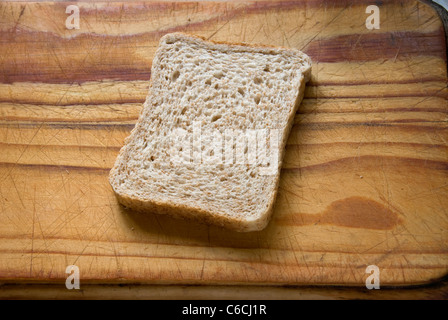 A slice of fresh brown bread on a wooden cutting board. Stock Photo