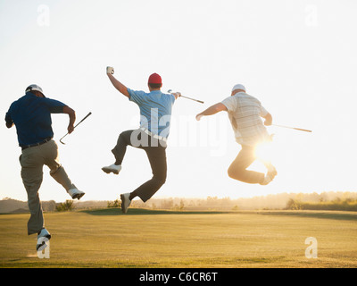 Excited golfers jumping in mid-air on golf course Stock Photo