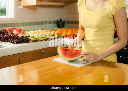 Mixed race woman cutting watermelon in kitchen Stock Photo