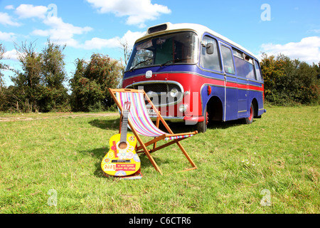 1971 Bedford camper van parked in a field, with an acoustic guitar and a deckchair in the foreground. Stock Photo
