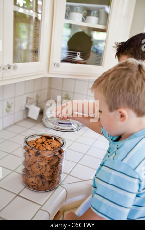 Caucasian brothers sneaking cookies in kitchen Stock Photo