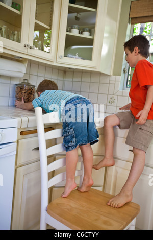 Caucasian brothers sneaking cookies in kitchen Stock Photo