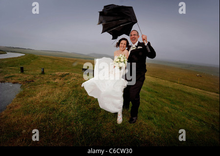 The pouring rain doesn't dampen happy couple Sandra and Scott's wedding as they pose on Beachy Head in strong winds. Stock Photo