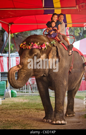 An Asian family rides on a costumed elephant at the amusement park of the Orange County Fair in Costa Mesa, CA. Stock Photo