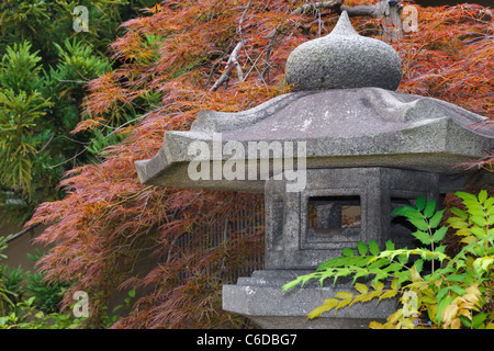 detailed image of Japanese stone lantern in zen garden with red maple tree on backward - focus on lantern Stock Photo