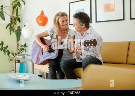 Man teaching wife to play guitar in living room Stock Photo