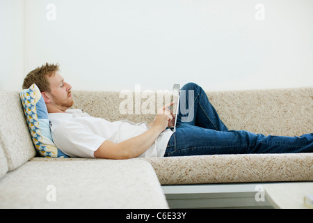 Caucasian man laying on sofa using digital tablet Stock Photo