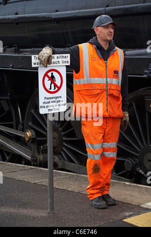 EWS railway crew leant against sign Trains run either way on each line Passengers must not pass this point or cross the line Stock Photo