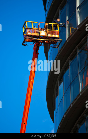England, London, Southwark. Workman performing maintenance from a cherry picker on a window of the London City Hall Stock Photo
