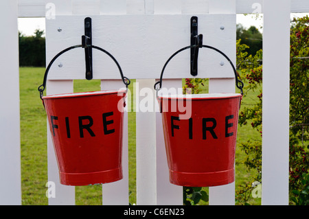 Two fire buckets hanging by hooks from a fence Stock Photo