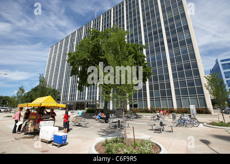 people at street hotdog vendor seller cart in plaza in front of office block downtown winnipeg manitoba canada Stock Photo