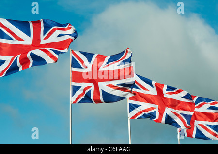 Four Union Jack flags flapping in the wind against a blue sky