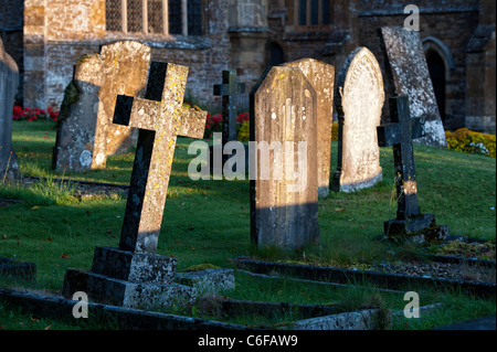 Cross headstones lit up in the early morning light. Kings Sutton, Nr Banbury, Northamptonshire, England Stock Photo