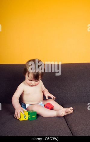A baby girl sitting on a sofa, playing with alphabet bricks Stock Photo