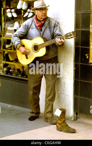 old man wearing cowboy hat and boots playing  guitar and ask for donations to be placed in his cowboy boot Stock Photo