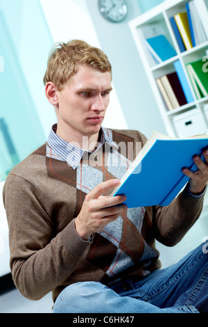 Image of serious student sitting on the floor and reading book Stock Photo