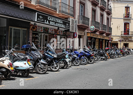 Motorcycles parked along narrow street in Seville Spain. Restaurant and cafe on edge of road. Stock Photo