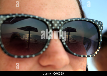 Reflections of the sea, beach and sunshade in teenagers sunglasses