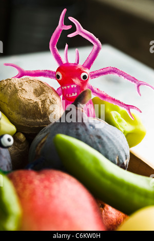 Toy monster in bowl of fresh vegetables and fruit Stock Photo